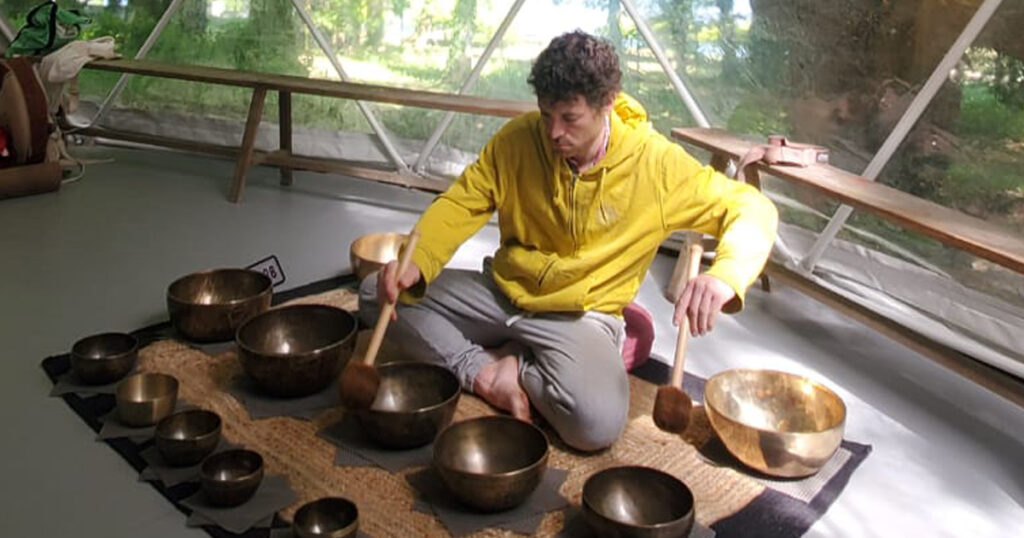 Grégoire Le Bris jouant des bols tibétains sous un dôme géodésique, professeur de yoga Vayu-Shanti, exposant au Festival bien-être de Pontourny 2026
